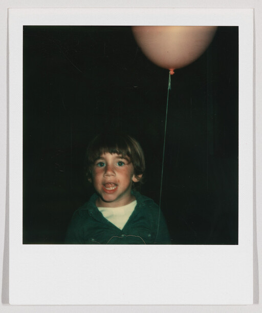 A young boy holding a string attached to a balloon while talking or shouting.