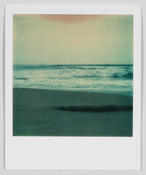 Waves crash onto a quiet sandy beach with a piece of driftwood near the shoreline.