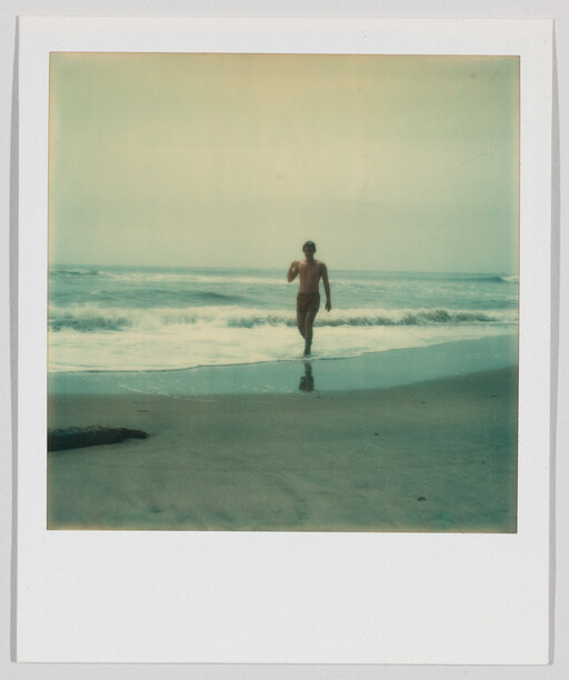 A man walks toward shore from the ocean with waves breaking behind him.