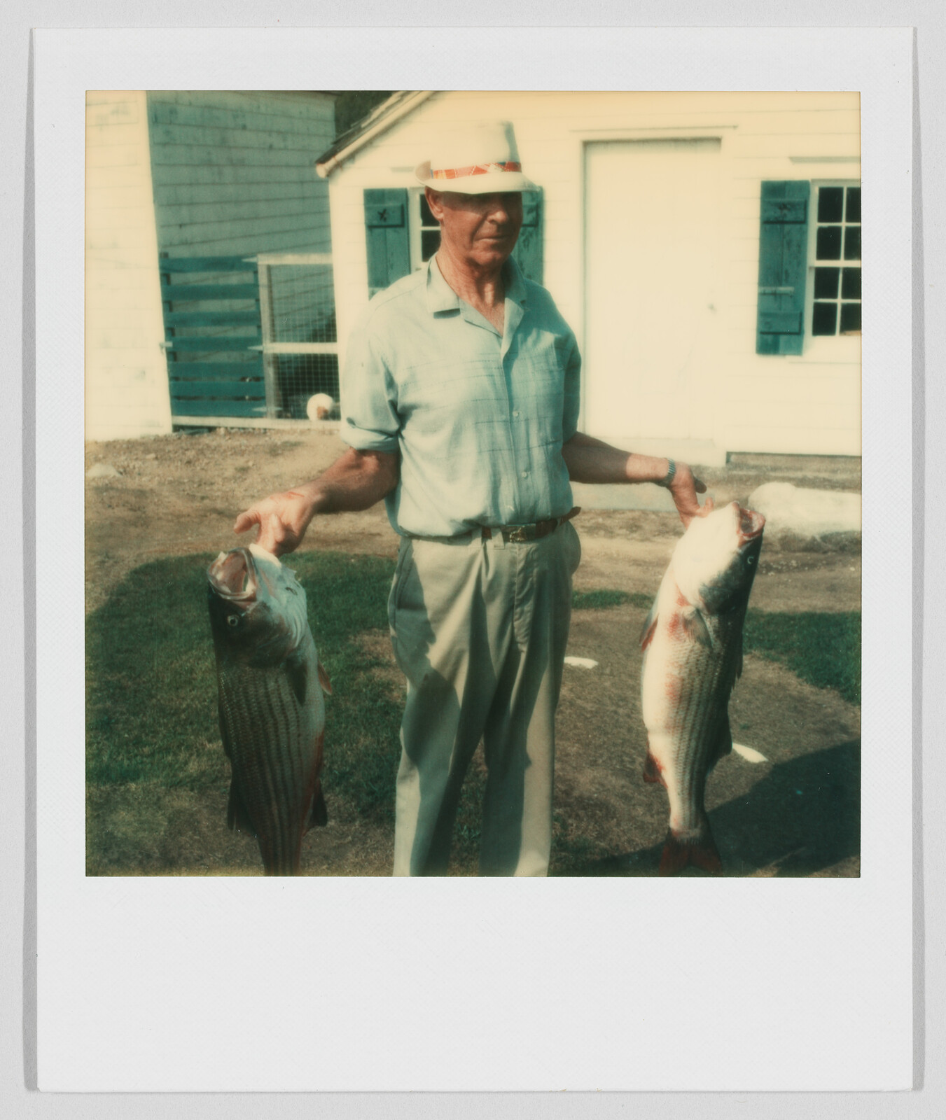 Man standing outside holding two large fish, one in each hand, in front of a white building.