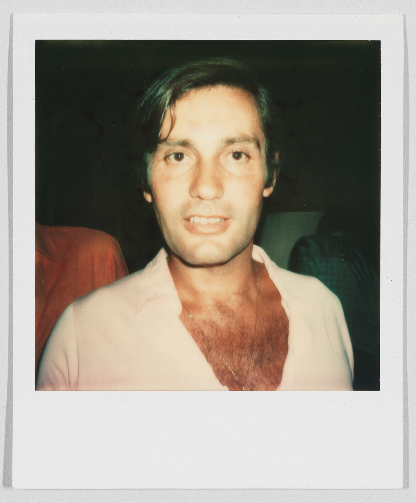 A man with short brown hair and an open-collared shirt looks directly at the camera, indoors.