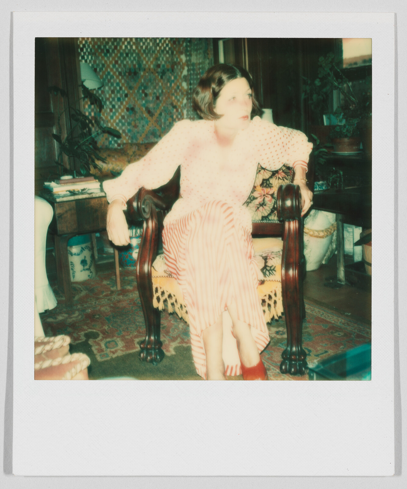 Woman with short hair sits on a wooden chair, wearing a light top and striped pants, looking sideways.