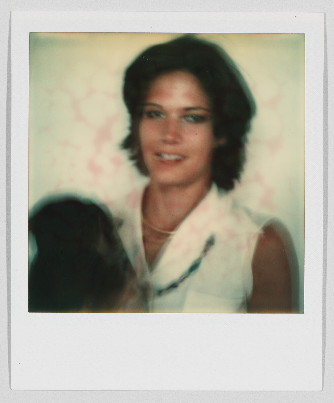 A person with short dark hair and a sleeveless shirt looks at the camera, image is slightly blurry.