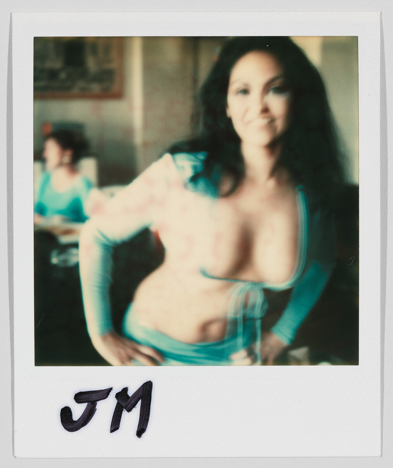 A woman in a revealing blue outfit poses with hands on hips; the initials "JM" are written below.
