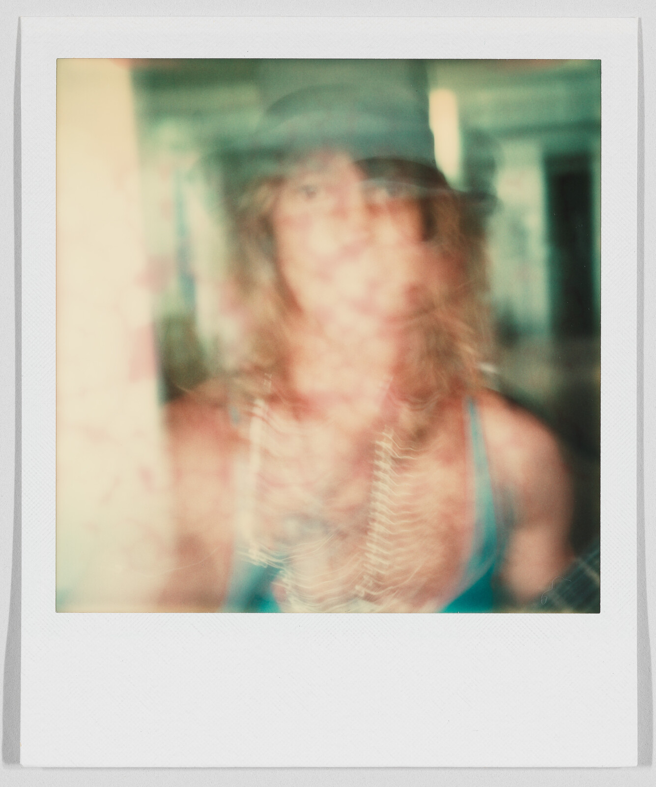 A person with long hair and a hat appears blurry, wearing a tank top and several necklaces.