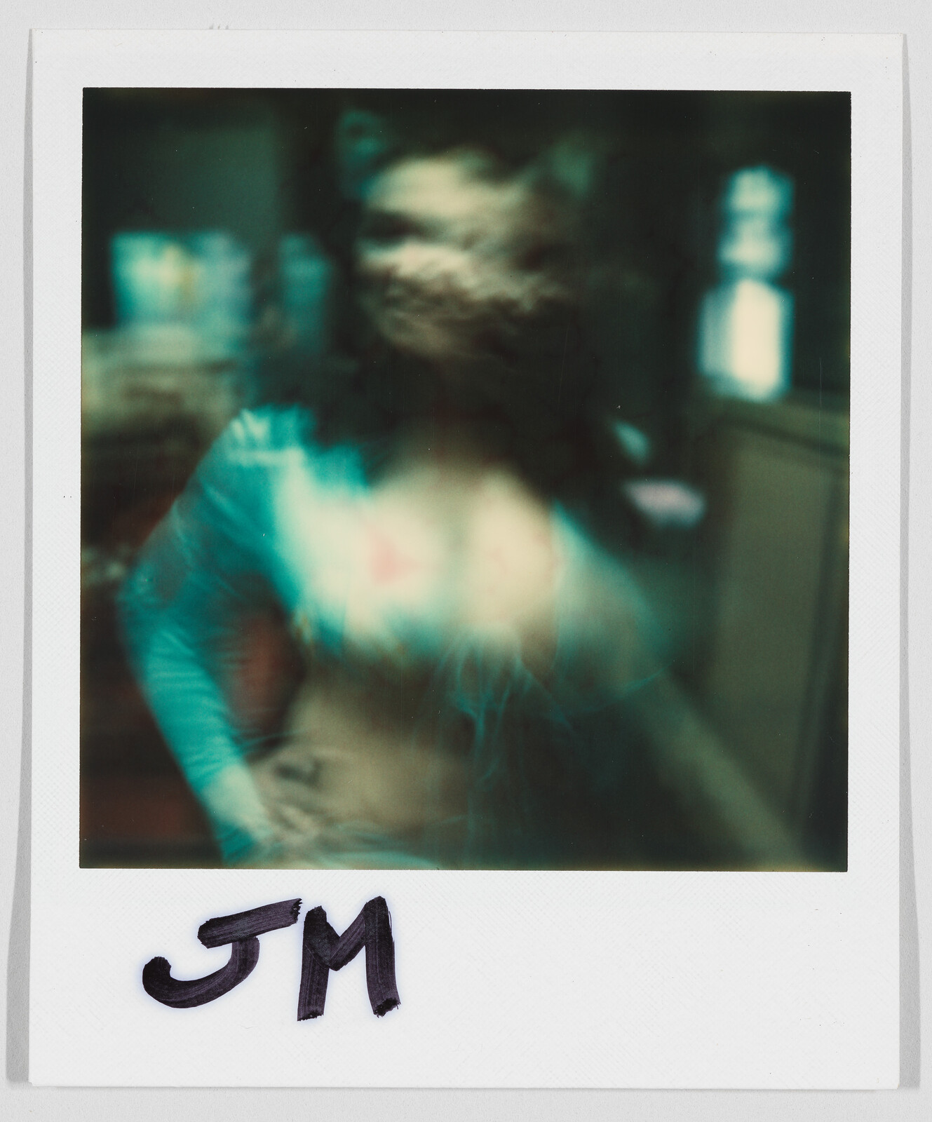 A blurry person stands indoors with “JM” written in black marker at the bottom of the photo.