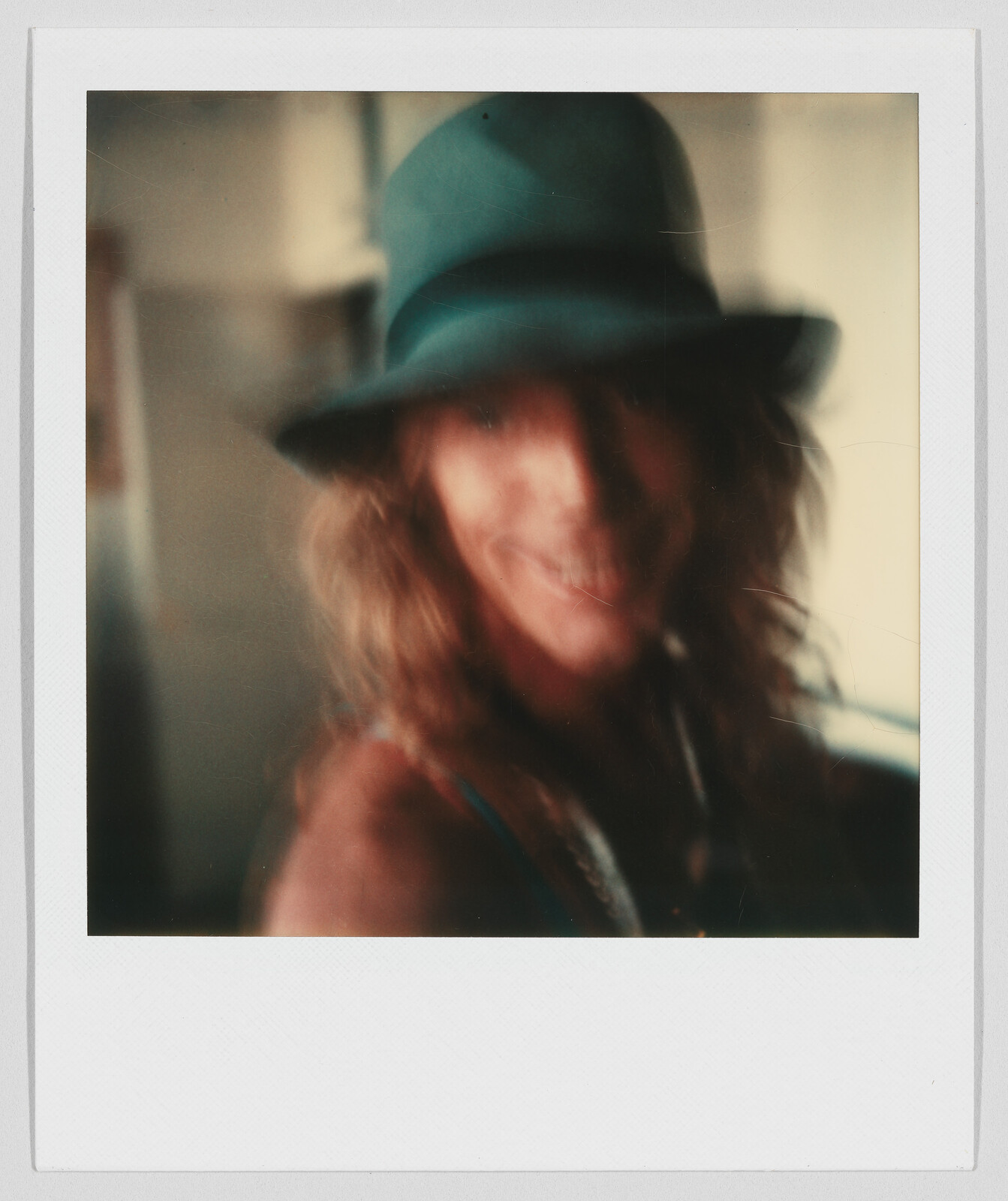 A person with long hair and a hat is smiling, but the image is very blurry and unclear.