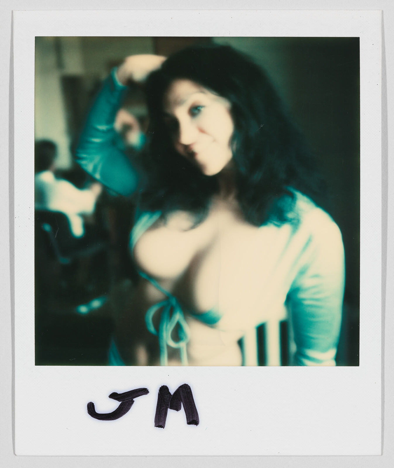 A woman with long dark hair poses indoors, wearing a low-cut top. The letters "JM" are written below.