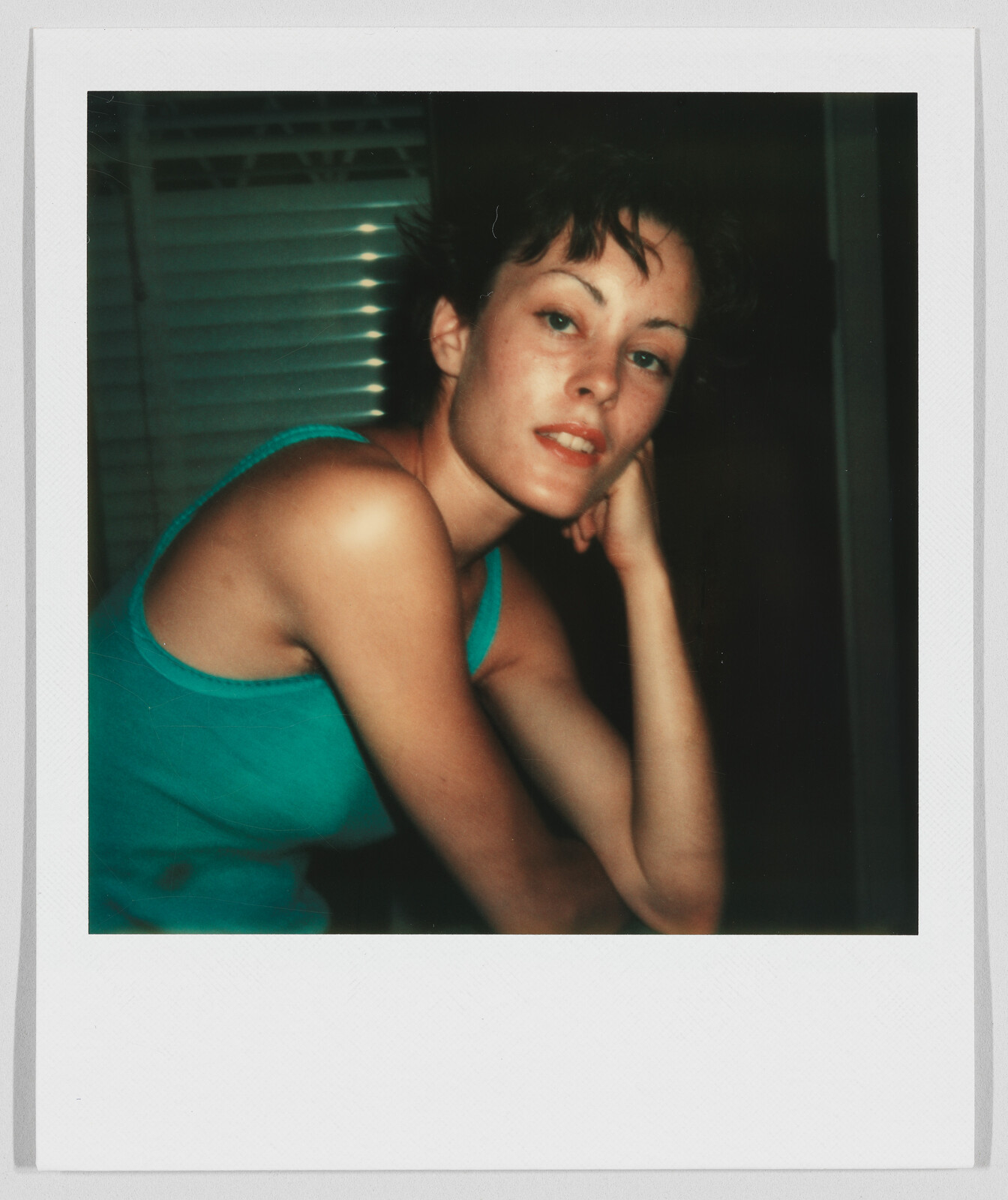 A person in a teal tank top rests their head on their hand, looking toward the camera.