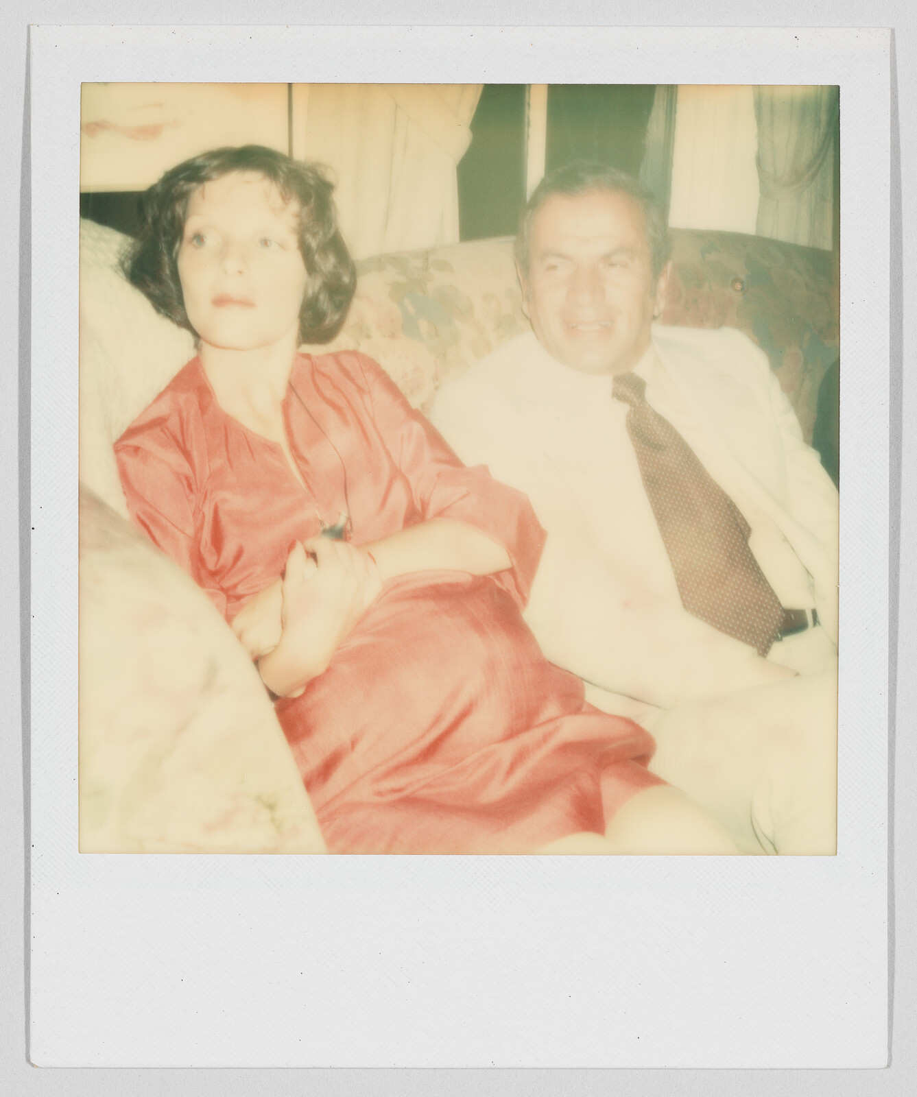 A woman in a red dress and a man in a white shirt sit together on a couch.