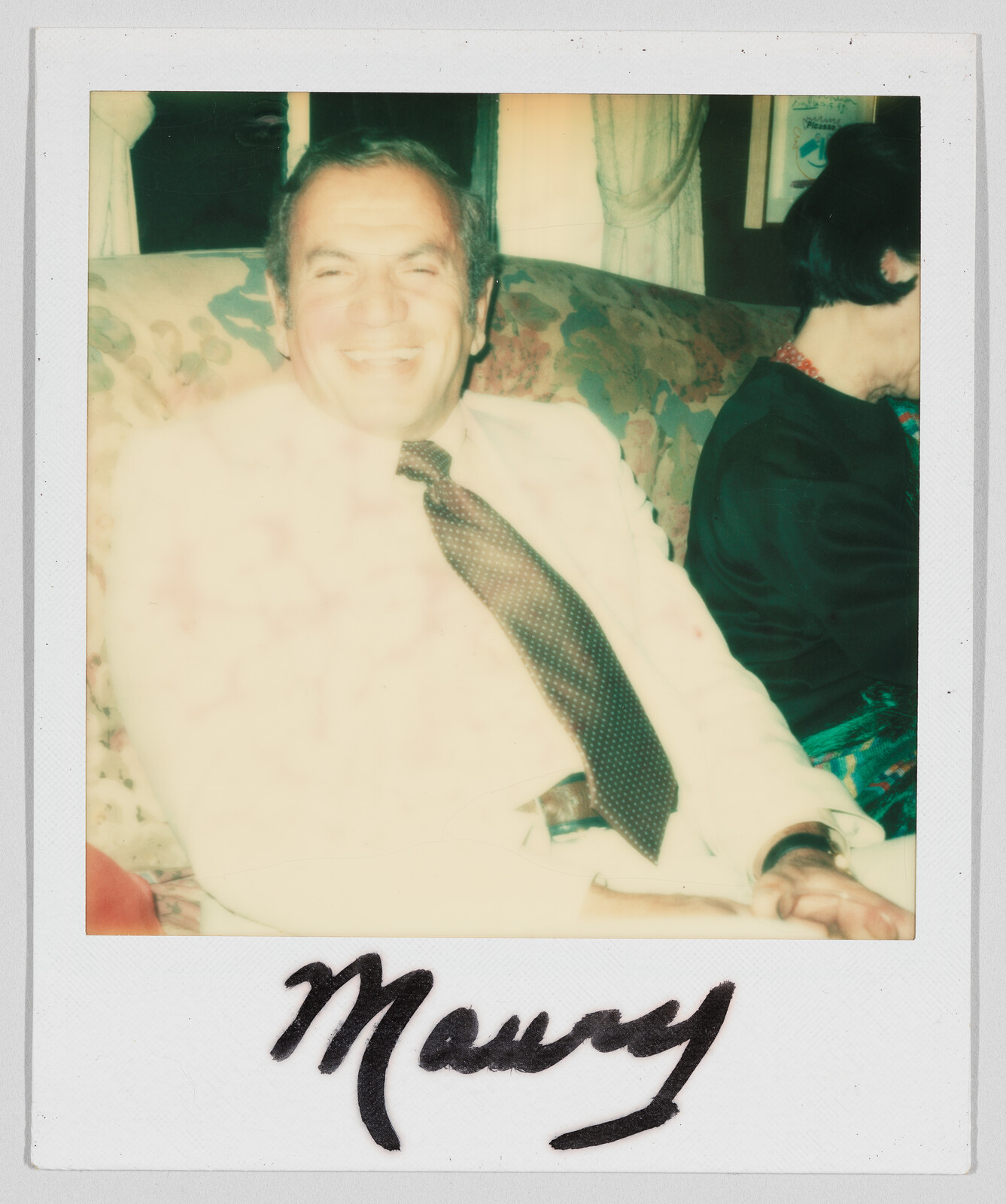 A man in a light suit smiles while sitting on a couch. The handwritten name "Maury" is below.