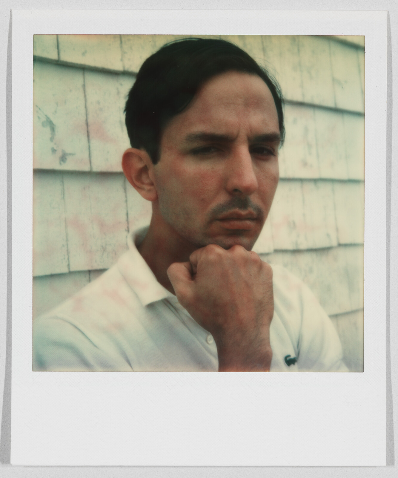 Man with short dark hair wearing a white shirt, resting his chin on his hand, looking serious.