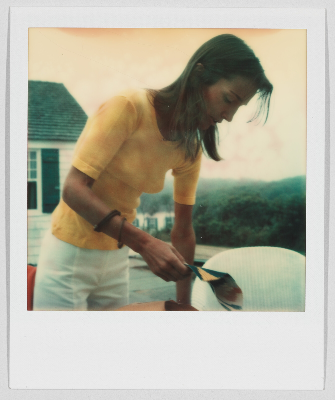 Woman in a yellow shirt serving food outdoors, leaning over a table with a spatula in hand.