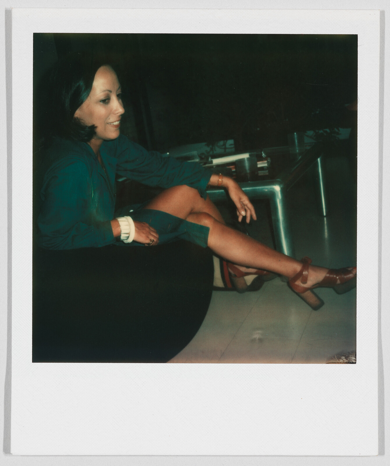 Woman sitting on a chair, smiling, with one leg crossed over the other and wearing a green outfit.