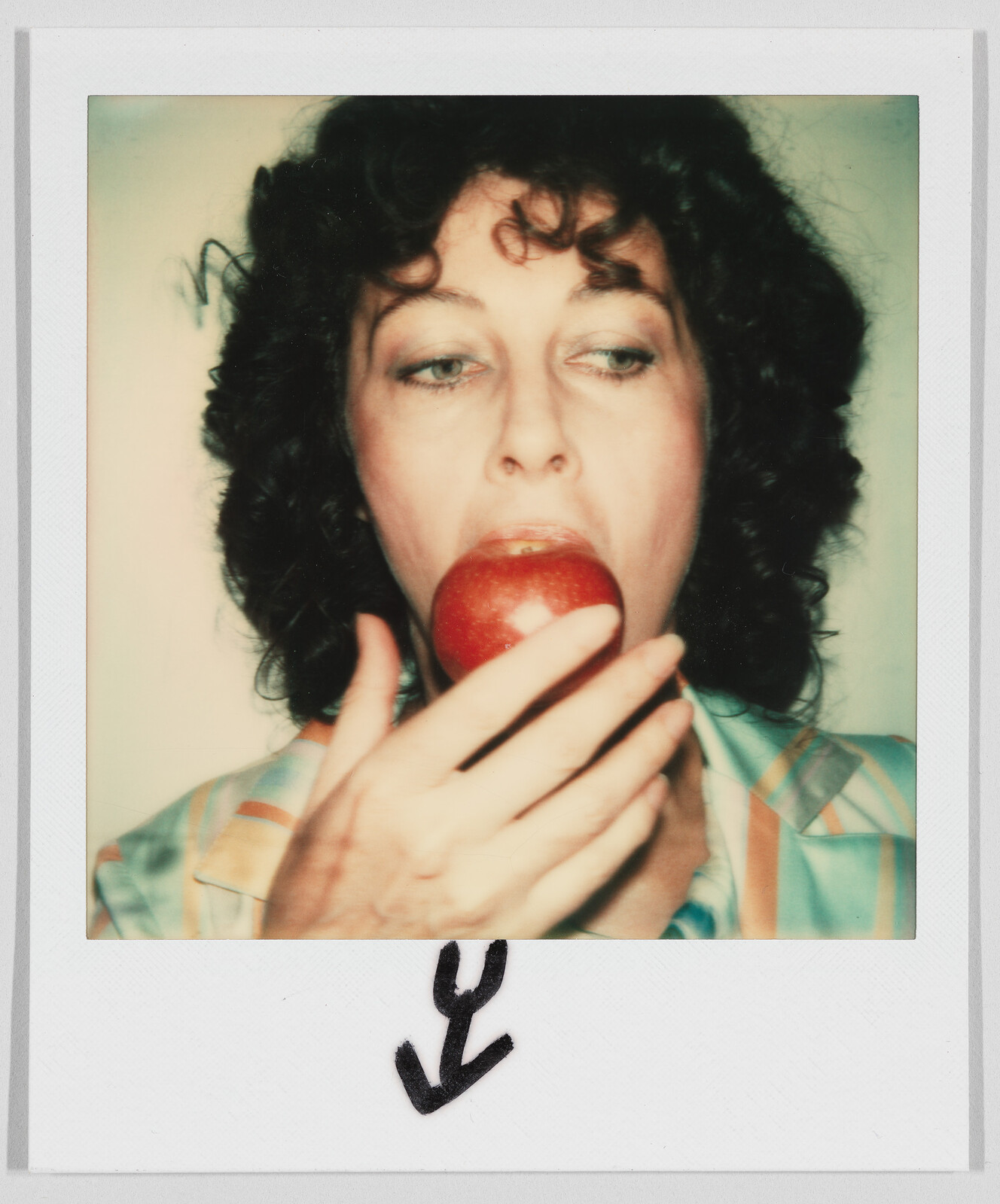Person with curly hair holding a red apple to their mouth, about to take a bite. Black arrow drawn below.