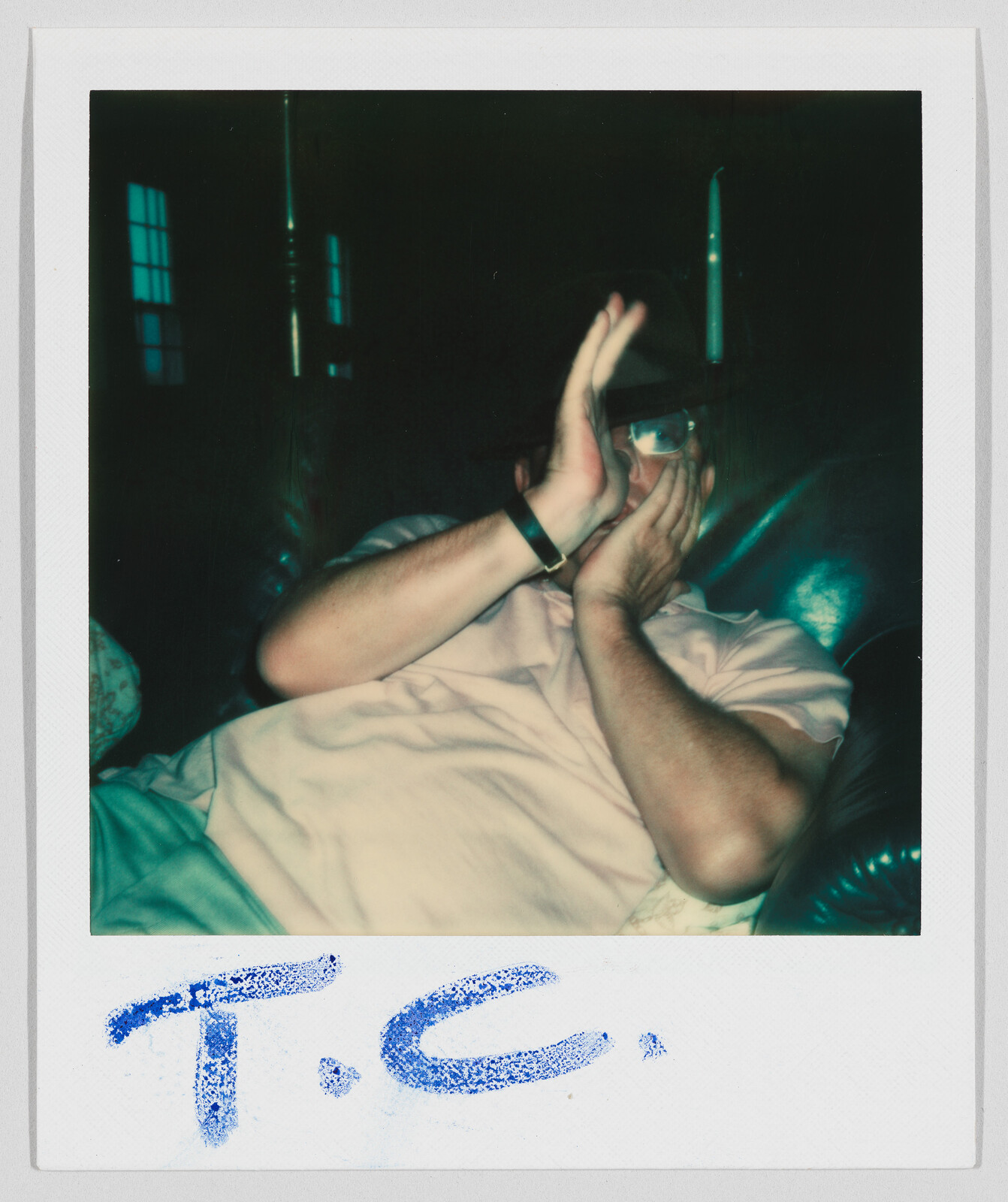 Person sitting on a couch covering their face with their hands; handwritten text below reads “T.C.”