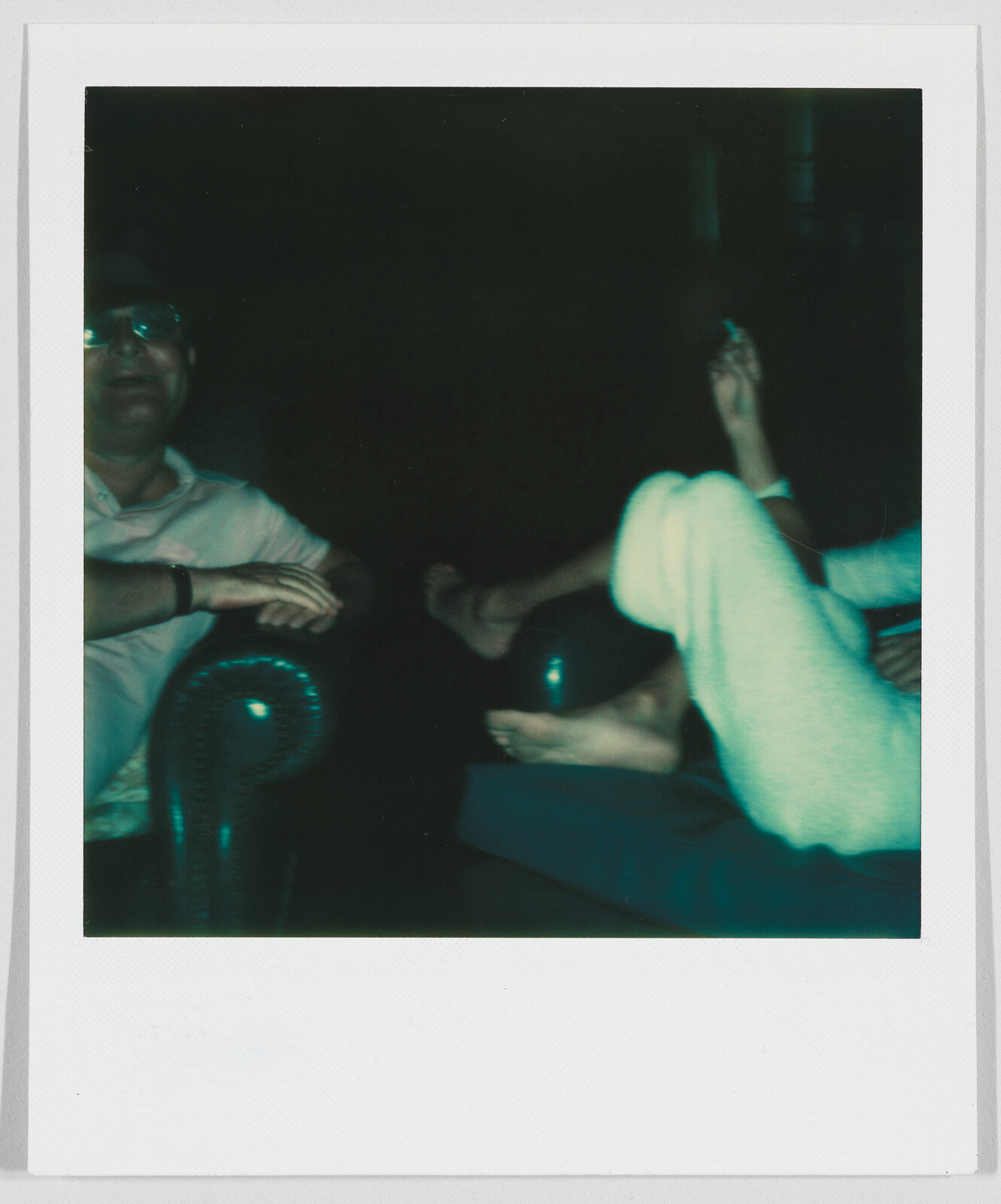 Two people relaxing on a couch in a dimly lit room, one person’s feet are visible and raised.