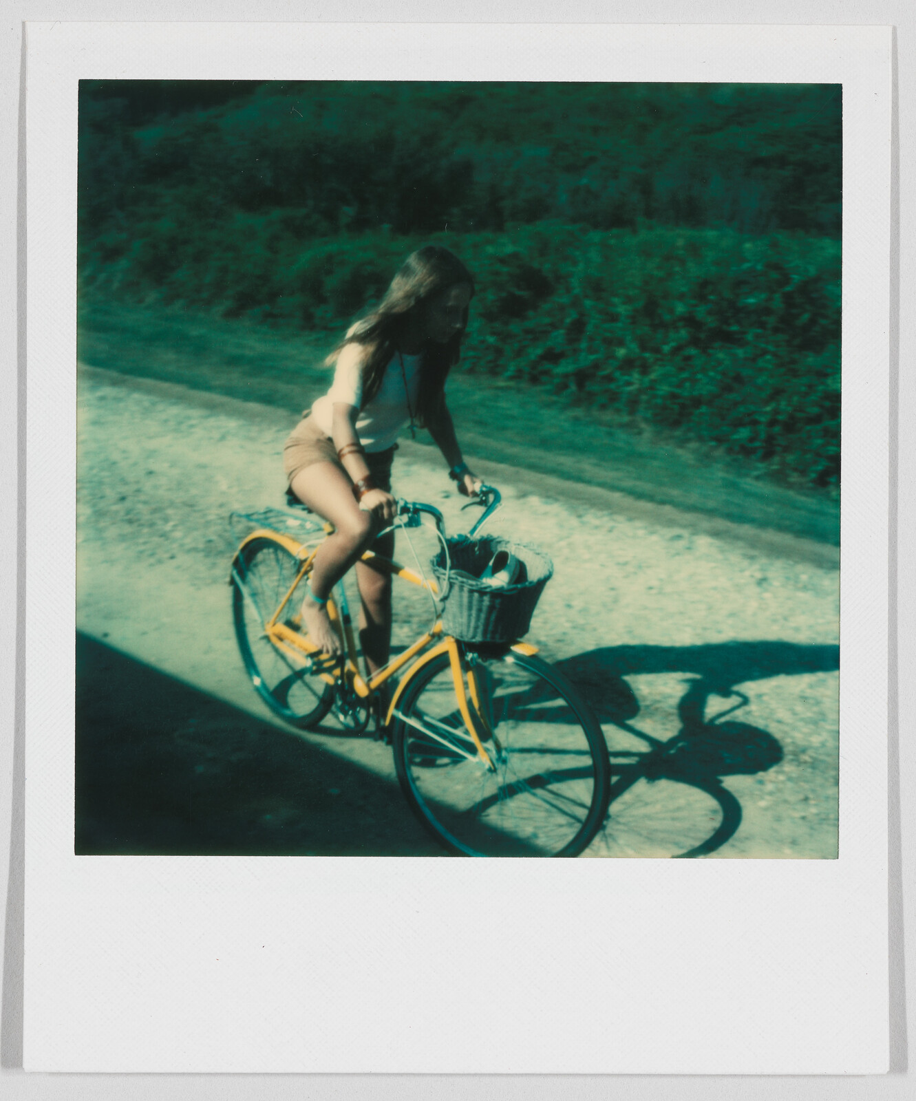 A young woman rides a yellow bicycle with a basket along a sunny, tree-lined path.