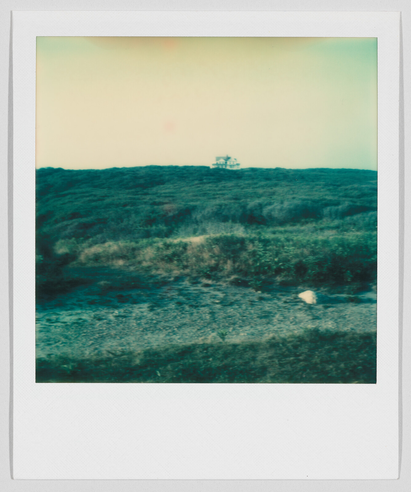 A small house sits alone on a distant hill, surrounded by grass and open land.