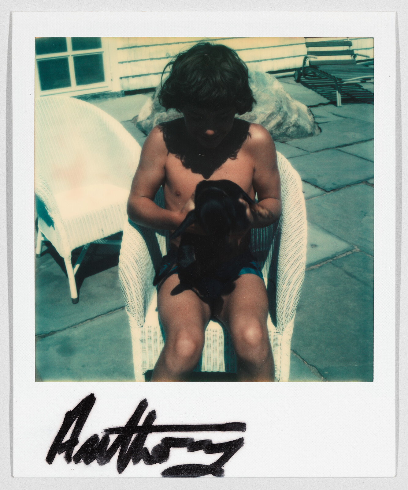 A shirtless child sits on a white chair outdoors, holding a small black dog. "Anthony" is written below.