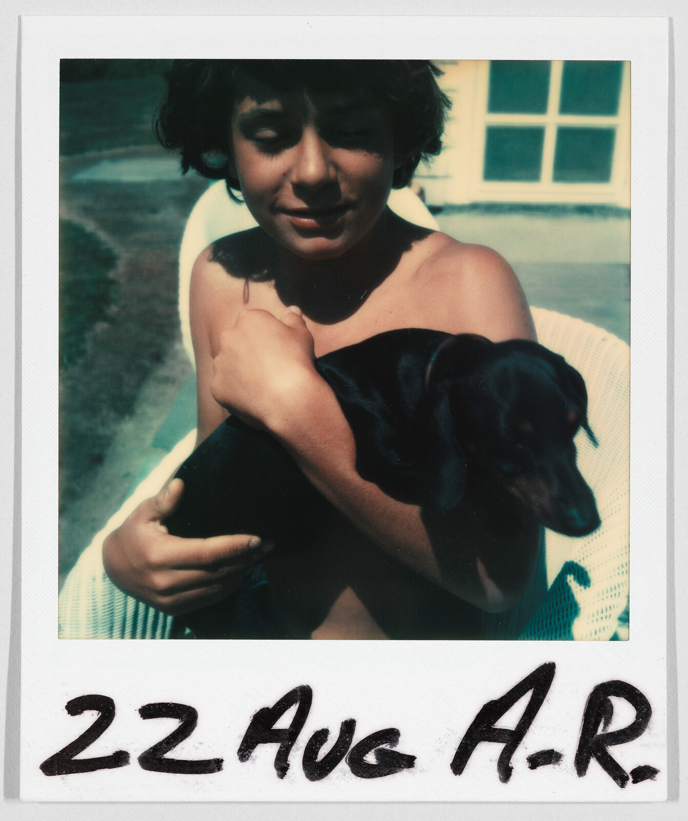 A young person sits outside holding a small black dog. Handwritten text at the bottom reads "22 Aug A.R."