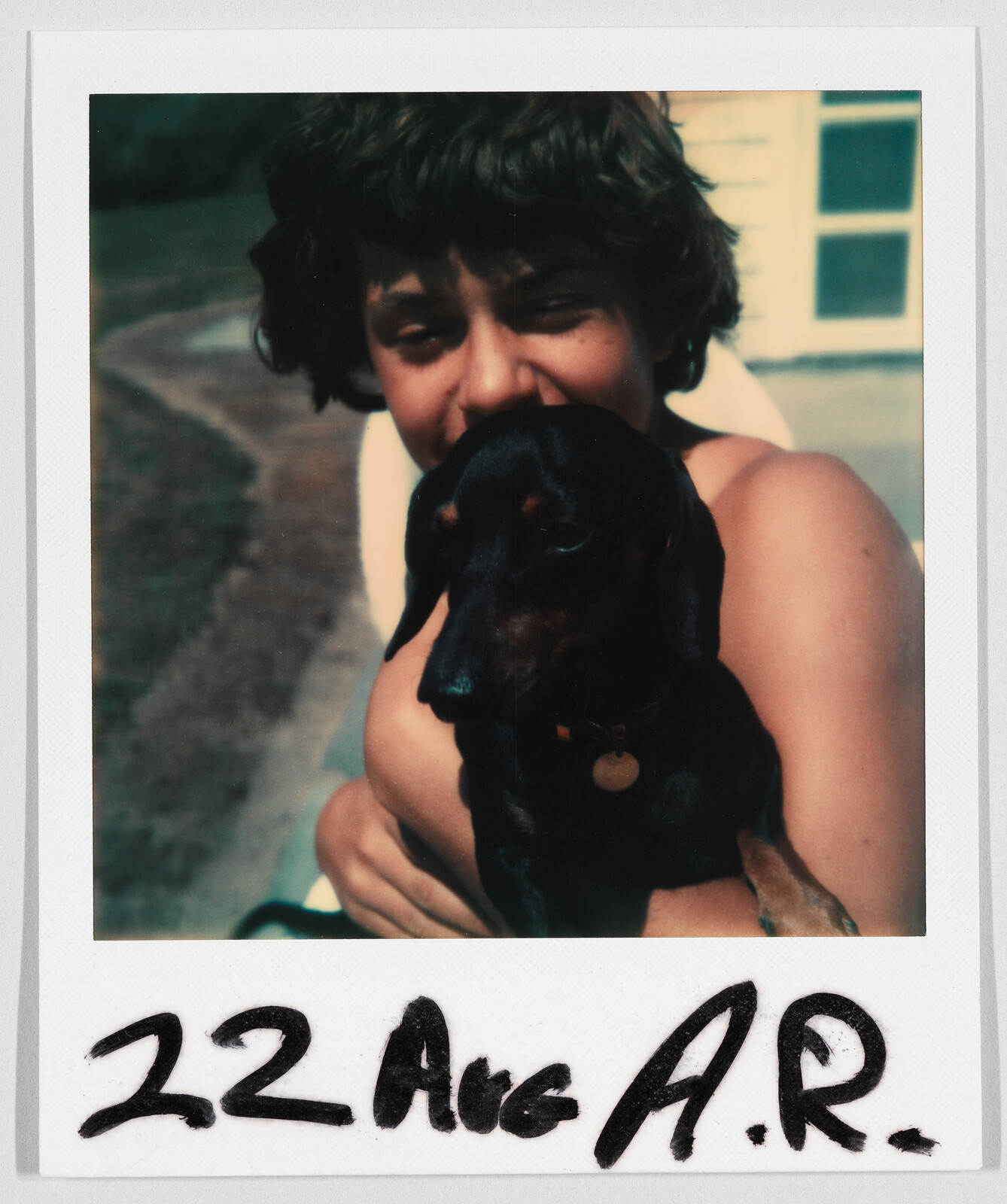 A person with short hair hugs a small black dog. Handwritten text at the bottom reads “22 Aug A.R.”
