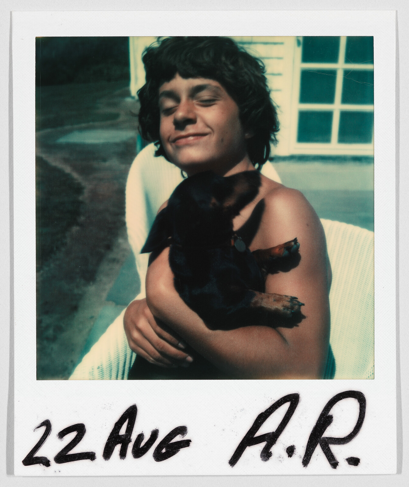 Smiling child sitting outside, holding a small black dog. Handwritten text at bottom reads “22 Aug A.R.”