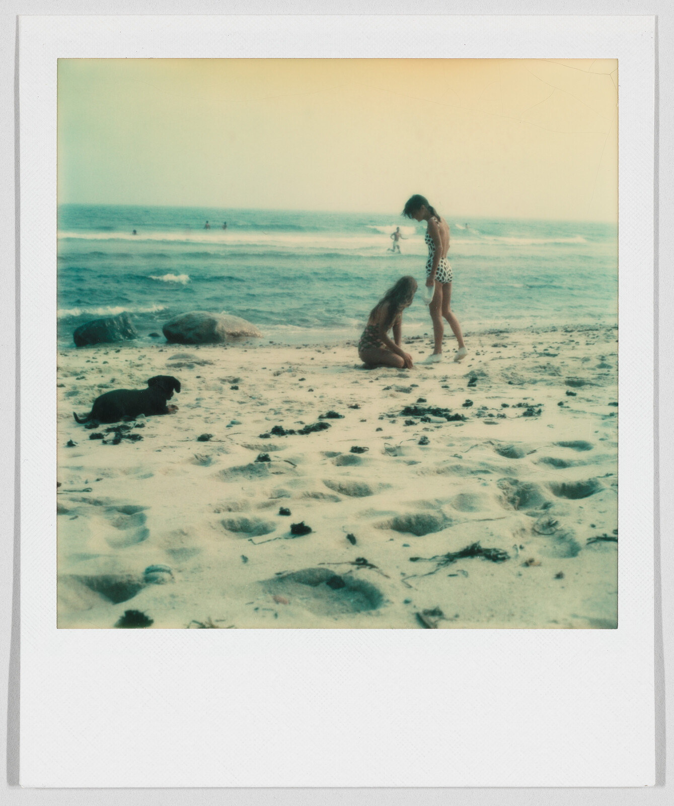 Two children play in the sand near the ocean, with a small black dog lying nearby.