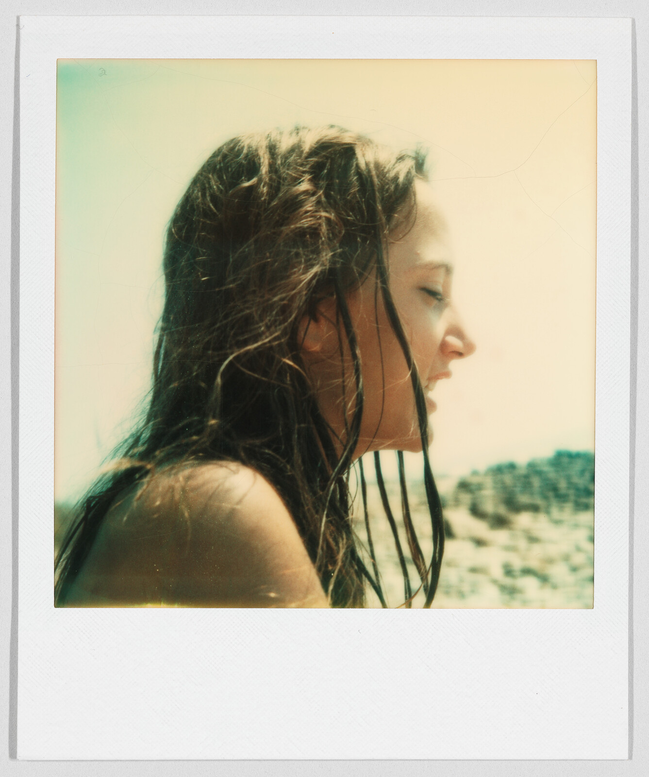 Young woman with wet hair looks to the side outdoors, with a bright sky and blurred landscape behind her.