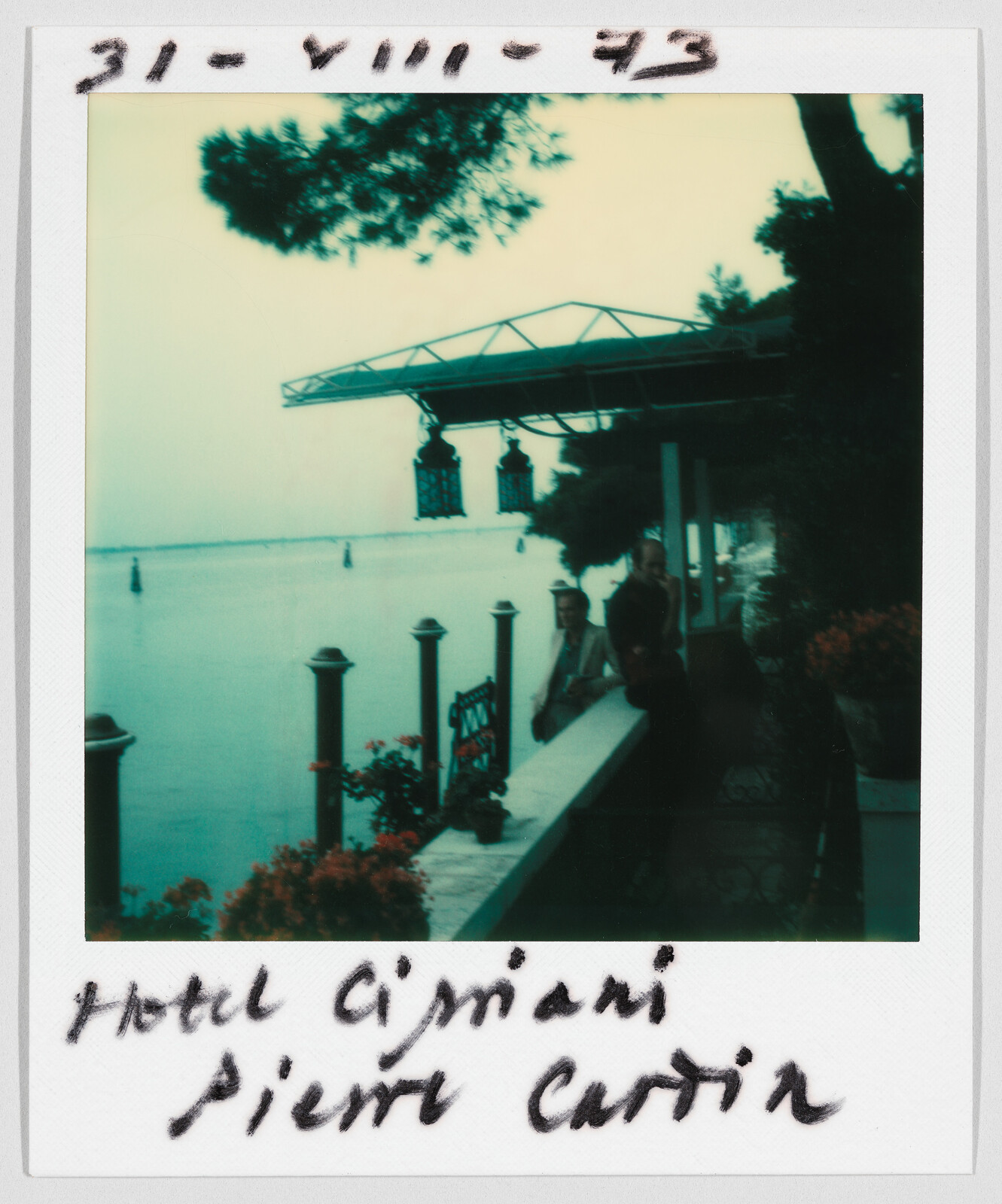 Two people stand by a waterfront terrace with flowers. Handwritten text reads “Hotel Cipriani Pierre Cardin.”
