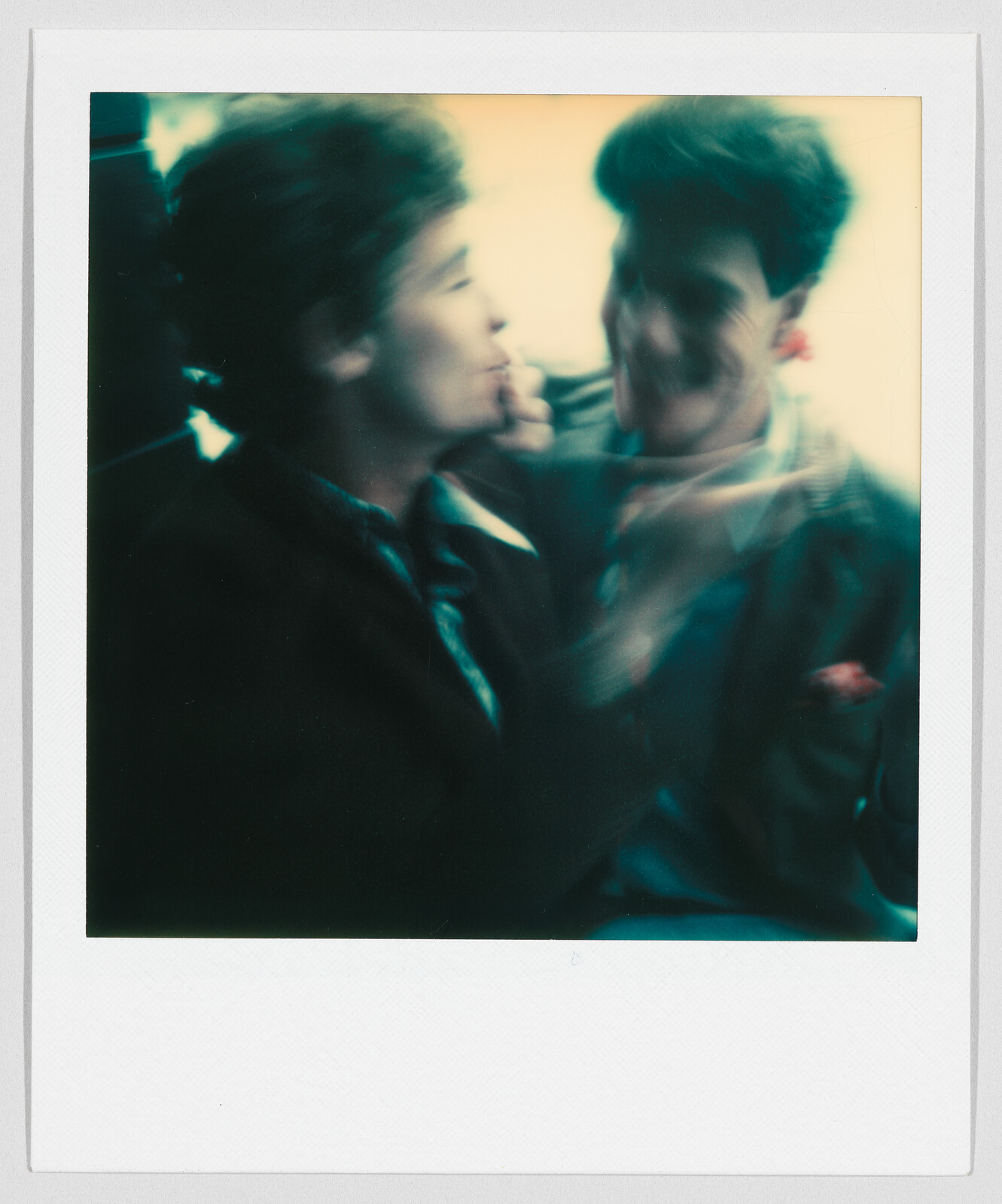 Two people with blurred faces are sitting close together, appearing to talk or interact with each other.