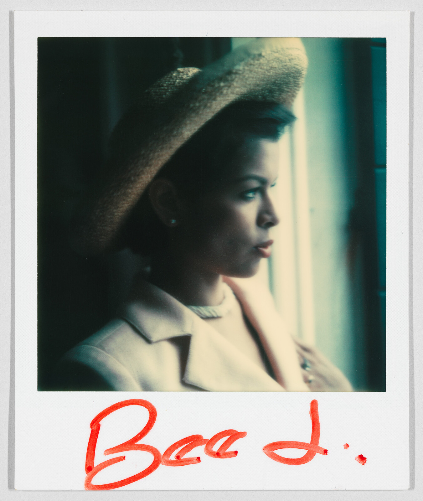 Person wearing a light-colored jacket and straw hat looks out a window; “Bee L.” is written in red.