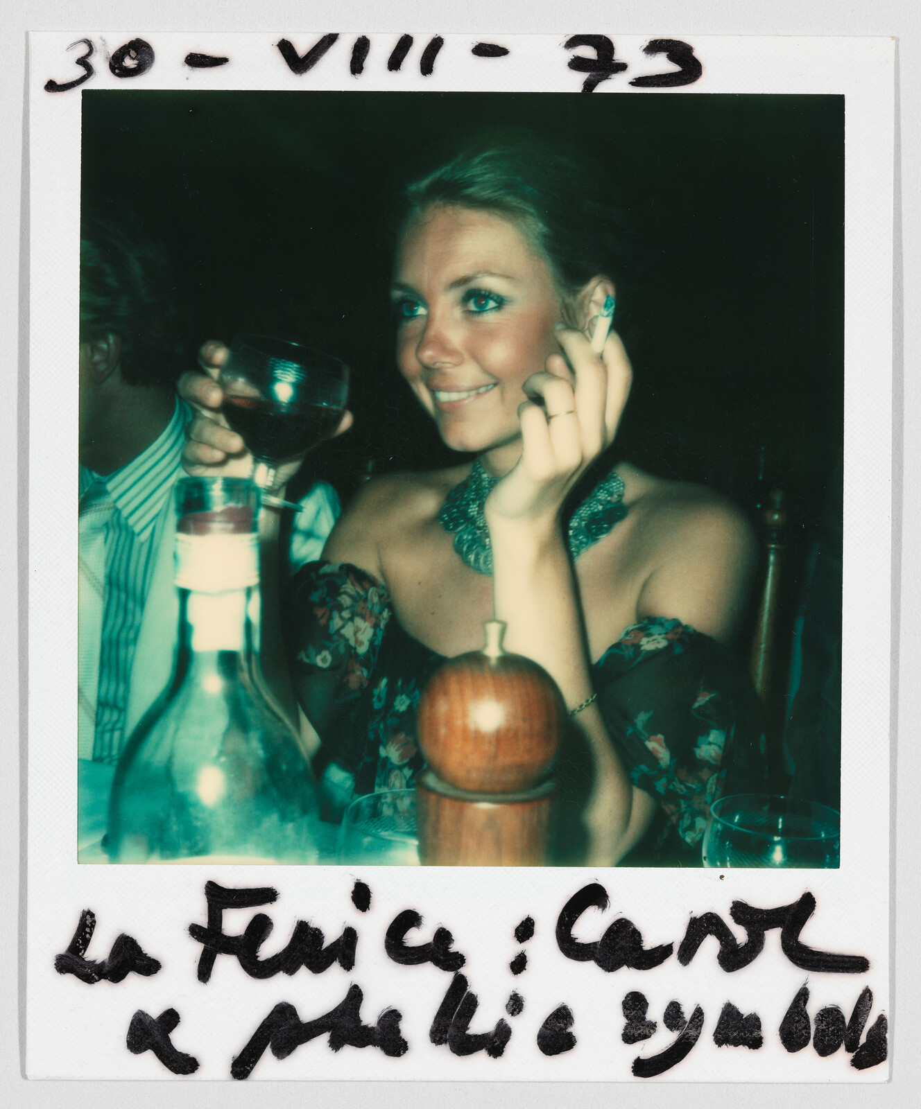 Woman smiling at a dinner table, holding a drink. Handwritten date at top: 30-VIII-73.