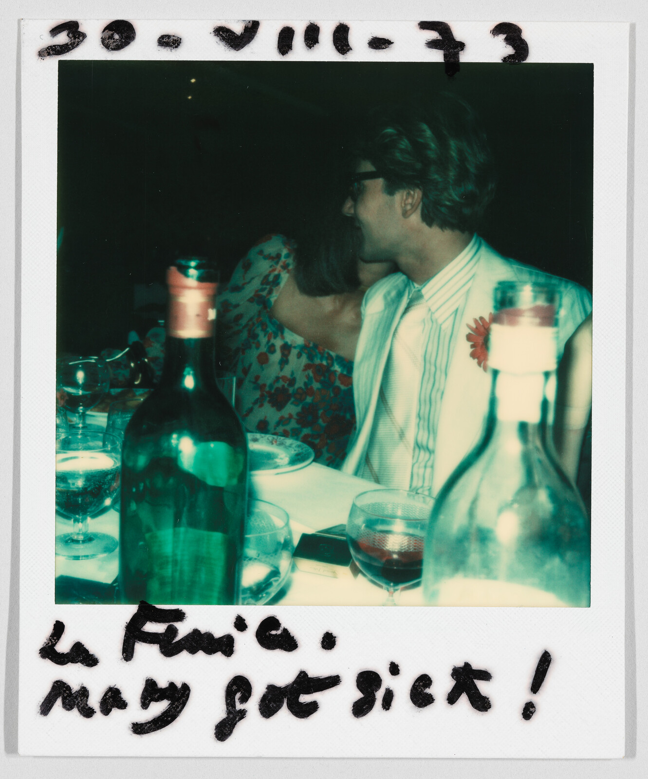 Two people sit close together at a dinner table with wine bottles; handwritten note says, “Mary got sick!”