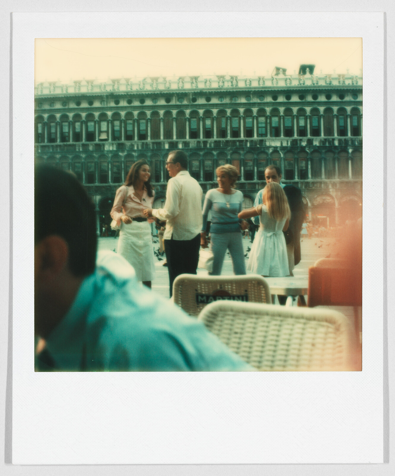 Four people stand and talk in a public square with a large historic building in the background.