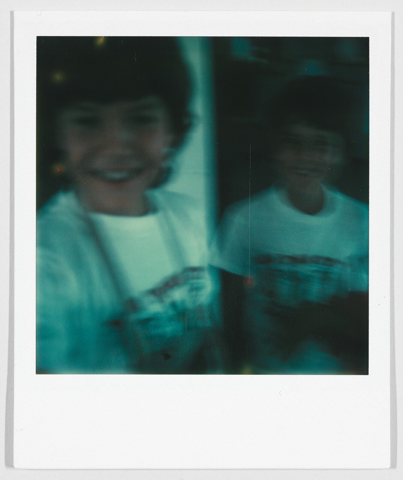 Two children with short hair wearing white shirts, both faces are blurry and hard to see clearly.