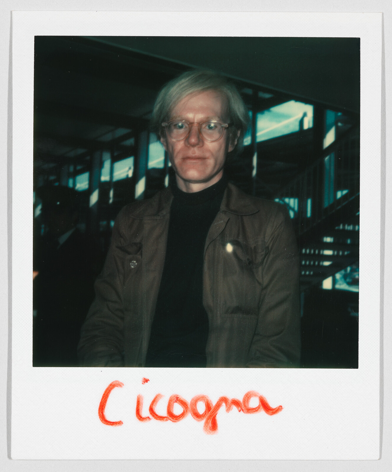 A person with light hair and glasses sits indoors; the word "Cicogna" is written in red below.
