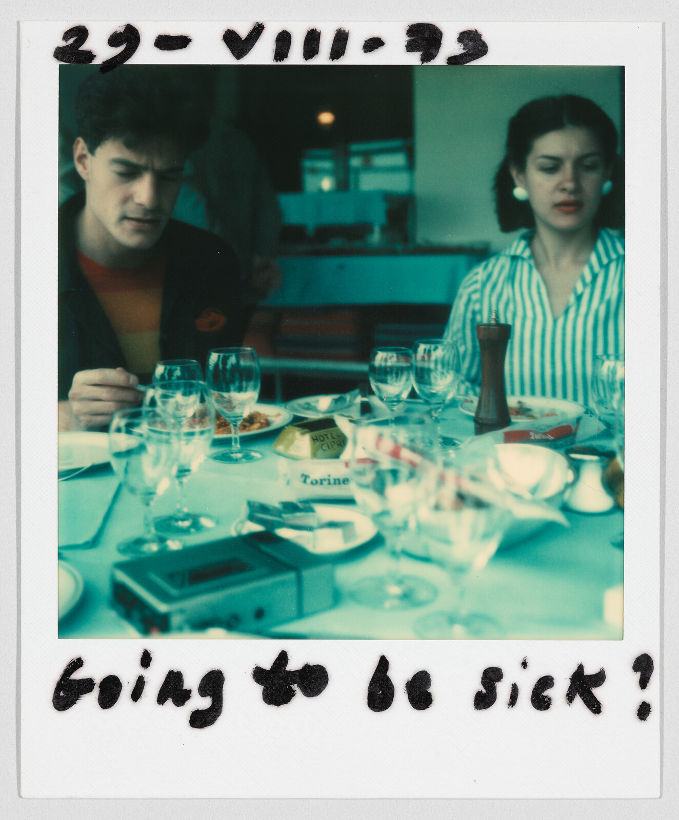 Two people sit at a table with food and empty glasses; handwritten text says "going to be sick?"