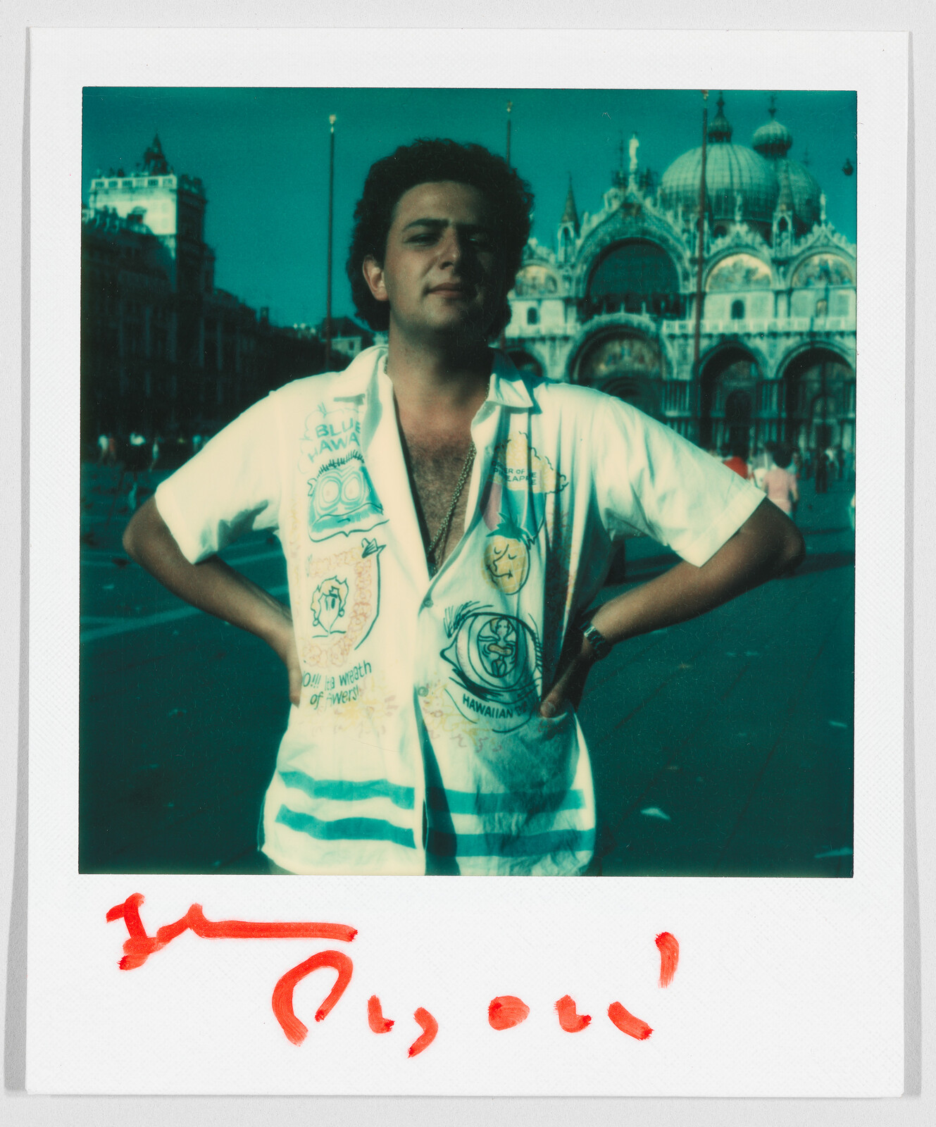 A person stands with hands on hips in front of a large, ornate building. Red handwriting is below.