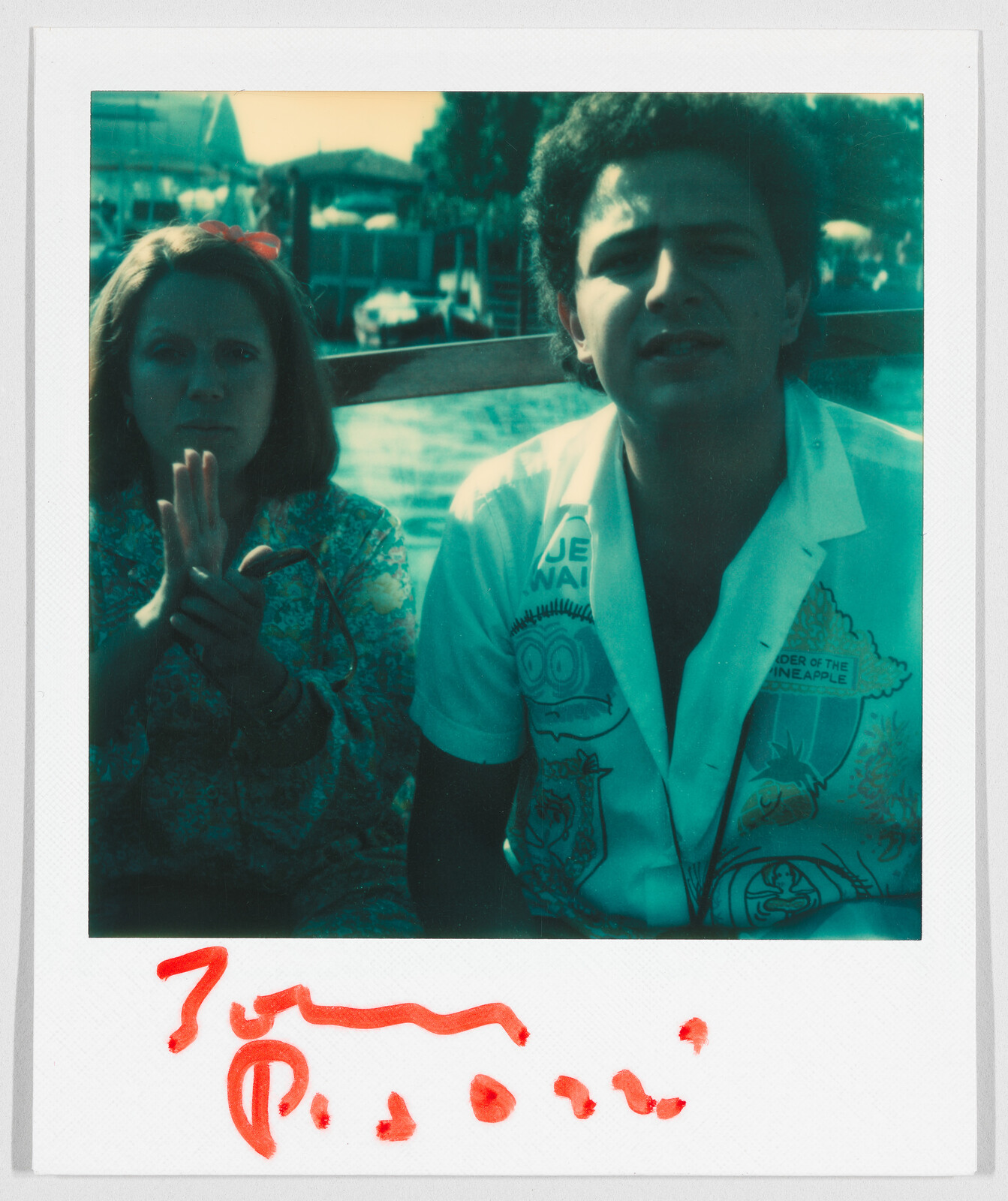 Two people sit close together outdoors; the man wears a shirt with cartoon drawings and visible text.