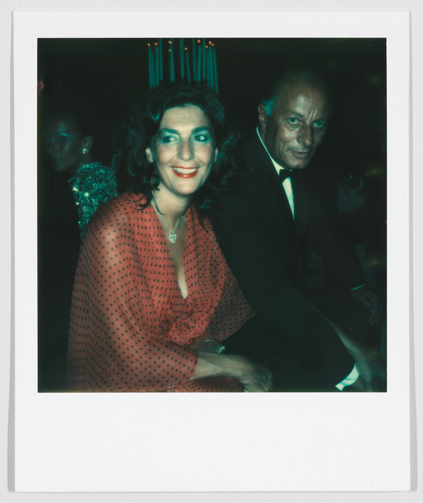 A woman in a red dress and a man in a suit sit together, both smiling at the camera.