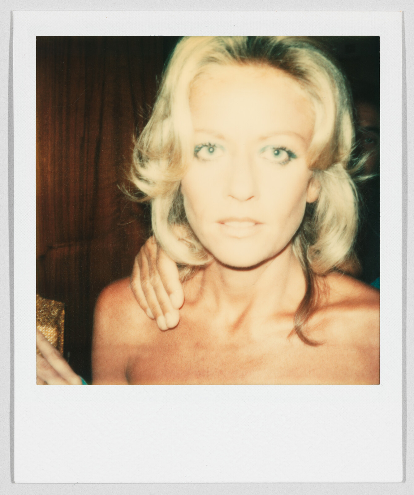 A woman with blonde hair looks at the camera, with a hand resting on her shoulder.