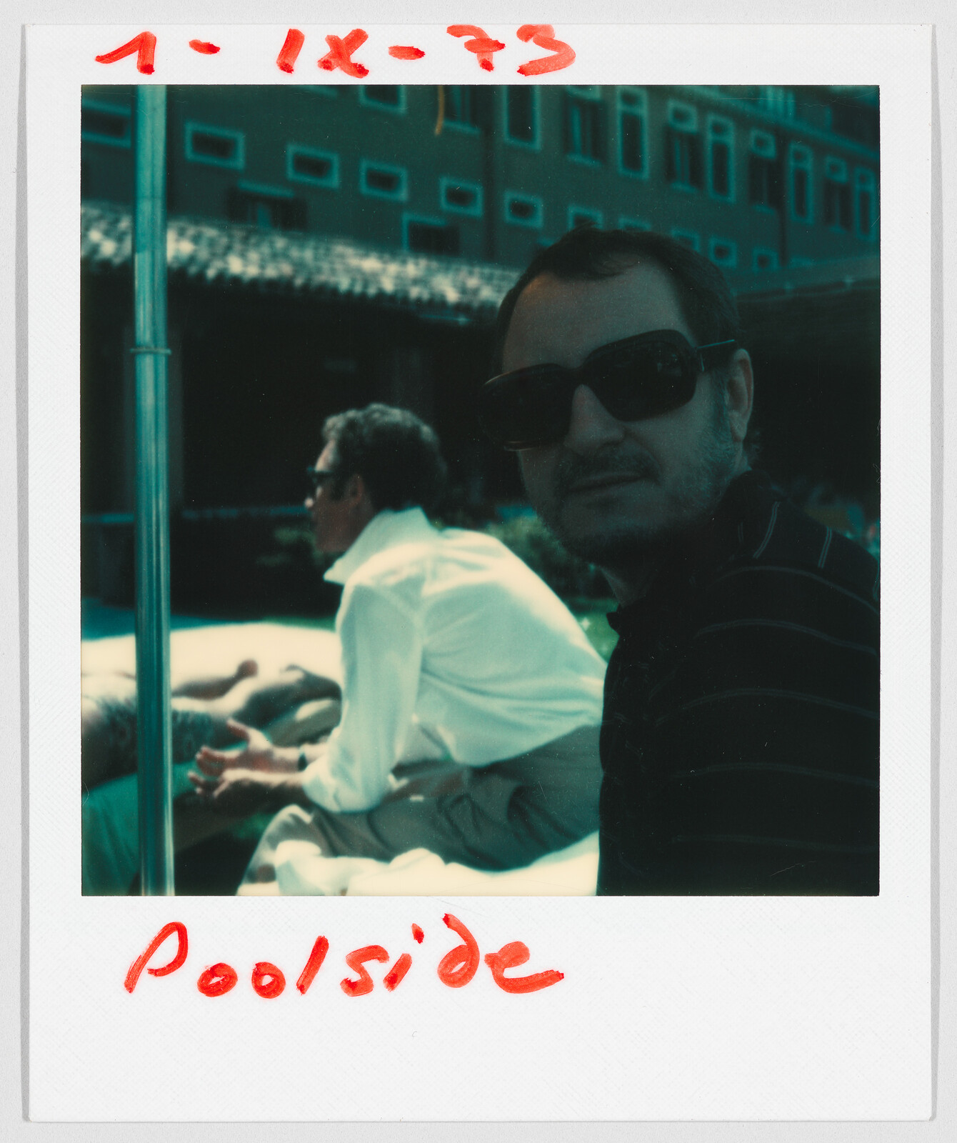 Two men sit by a pool, one wearing sunglasses. Handwritten text says “Poolside” and “1-IX-73.”