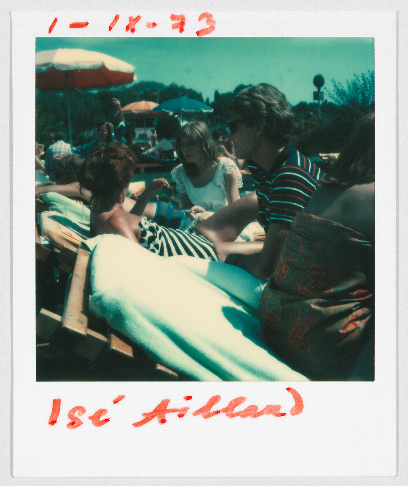 Several people relax on lounge chairs under umbrellas outdoors. Red handwritten text at the top reads "1-IX-73".