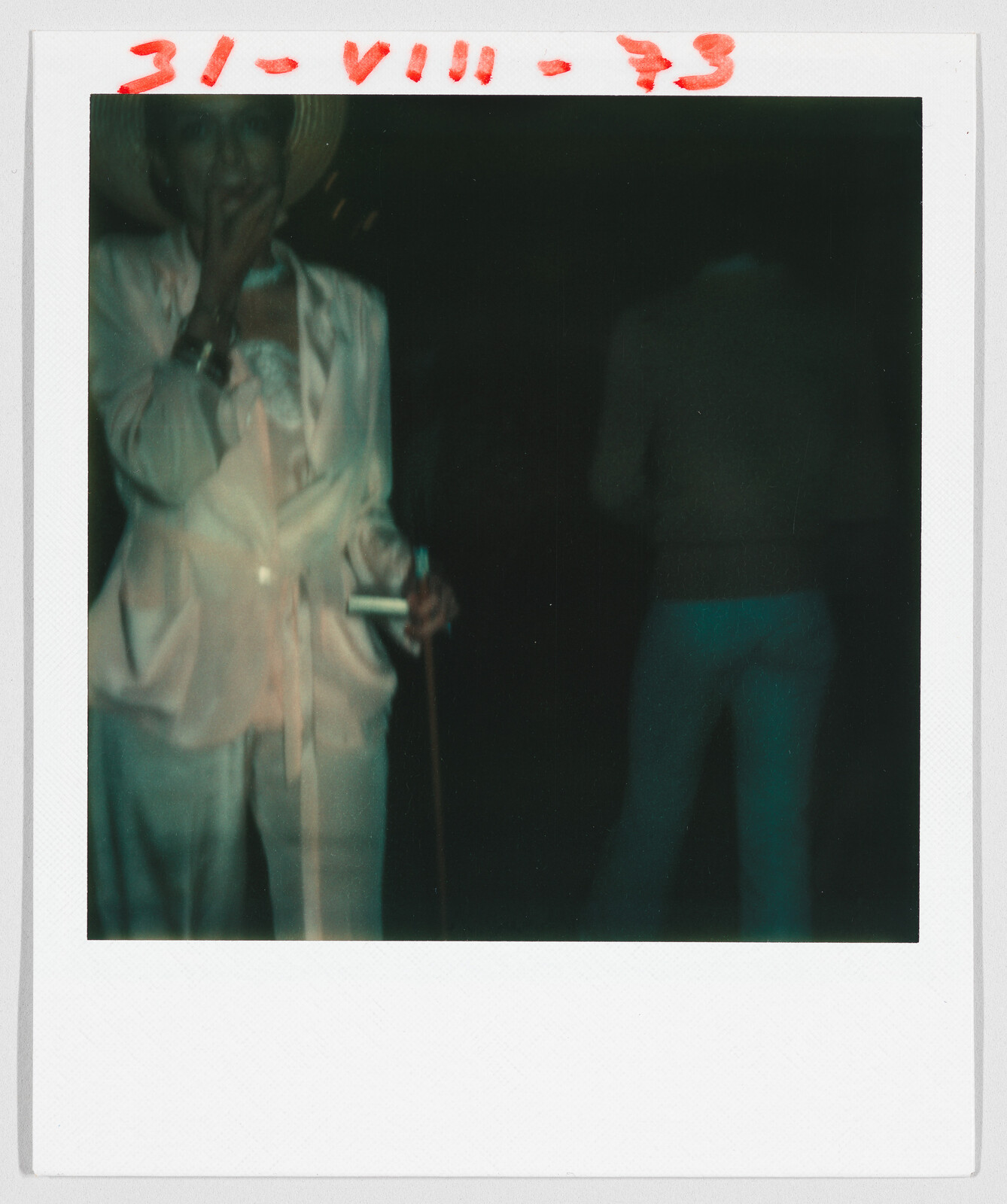 Person in light clothing holding a cigarette, with handwritten date "31-VIII-73" in red at the top.