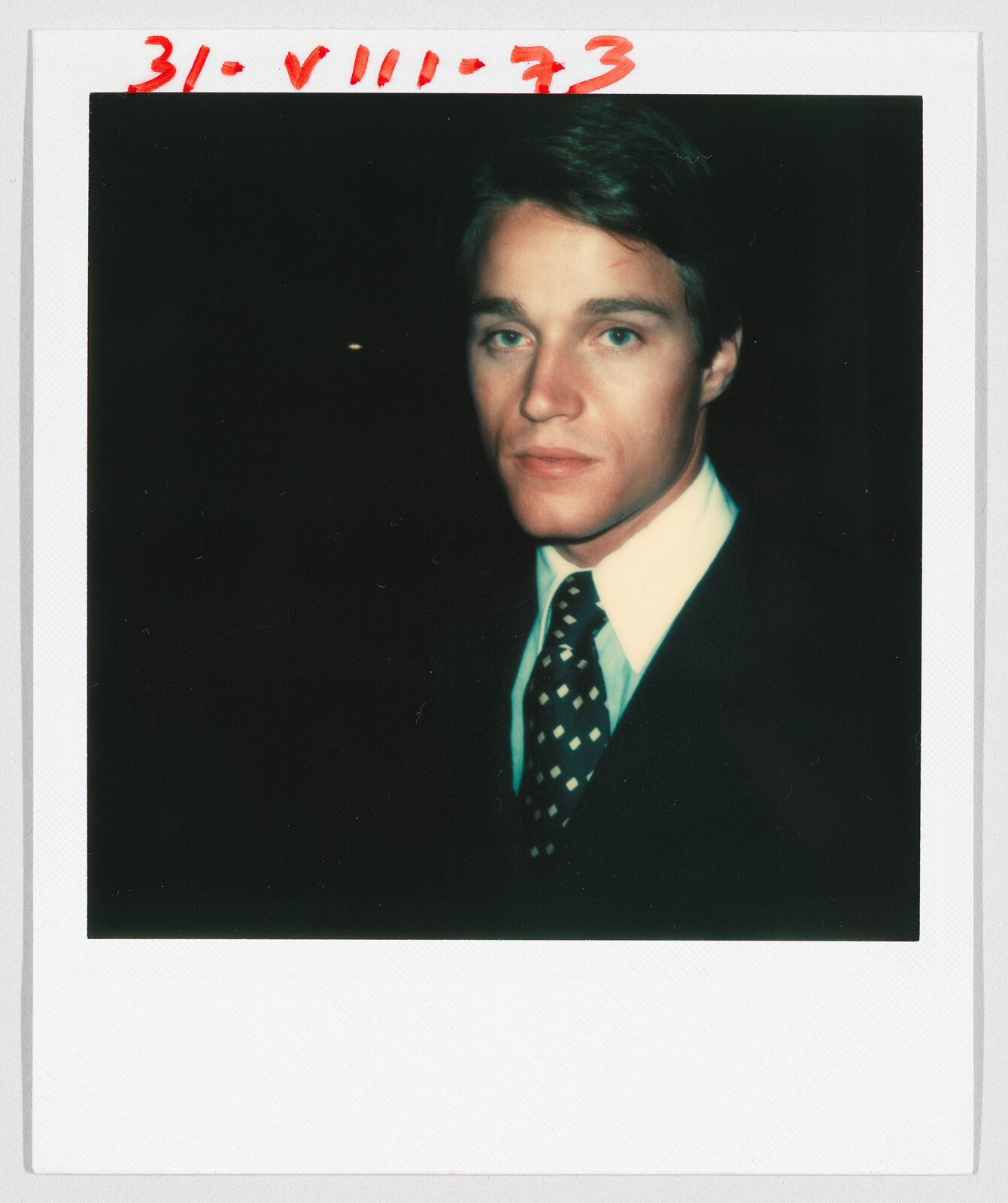 A young man in a suit and tie looks at the camera; handwritten date “31-VIII-73” at the top.