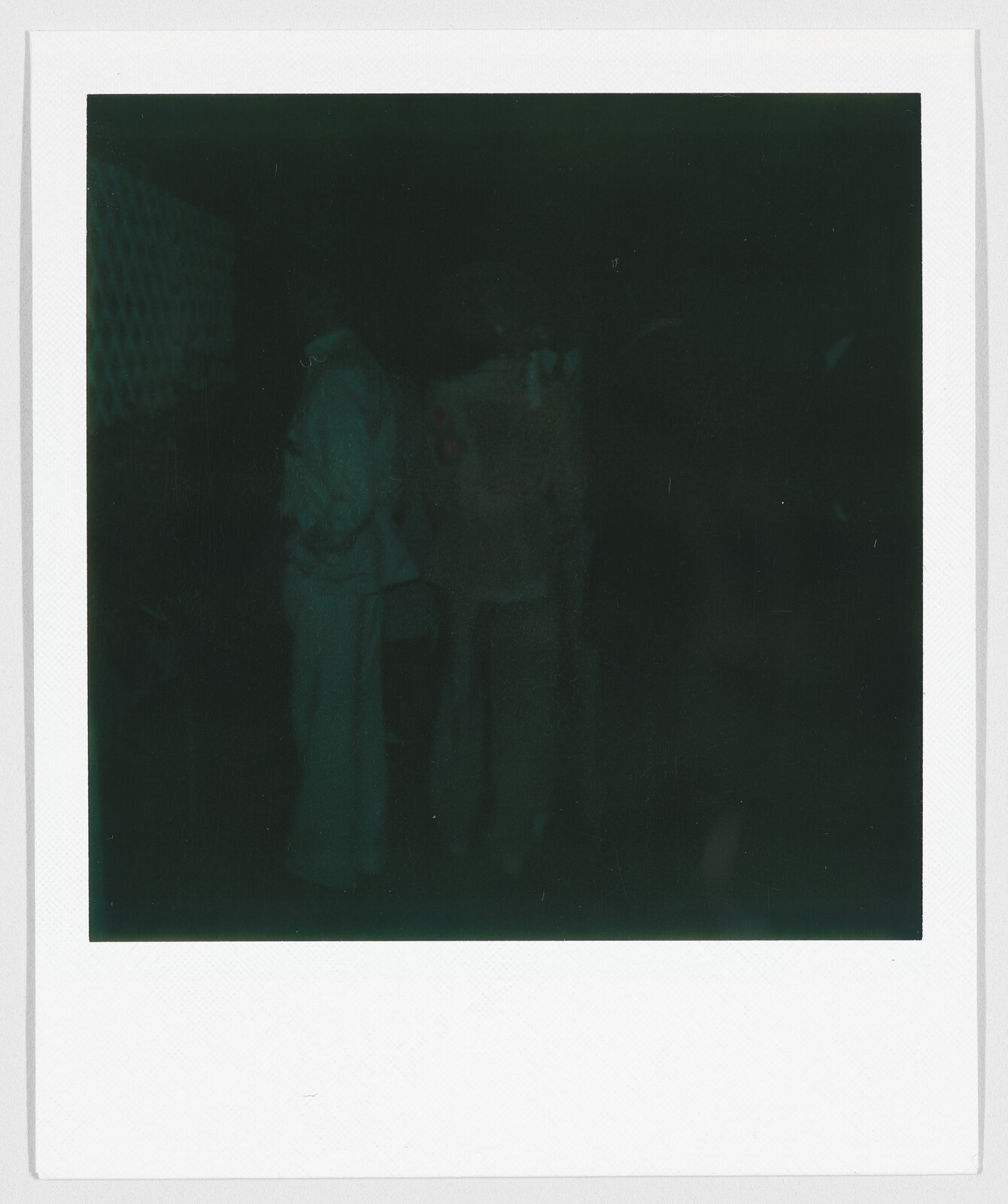 Two people standing together in a very dark setting, with details difficult to see clearly.