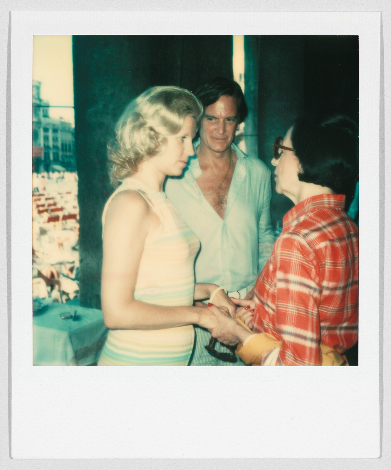 Three adults stand together indoors, two women holding hands and talking while a man looks on and smiles.