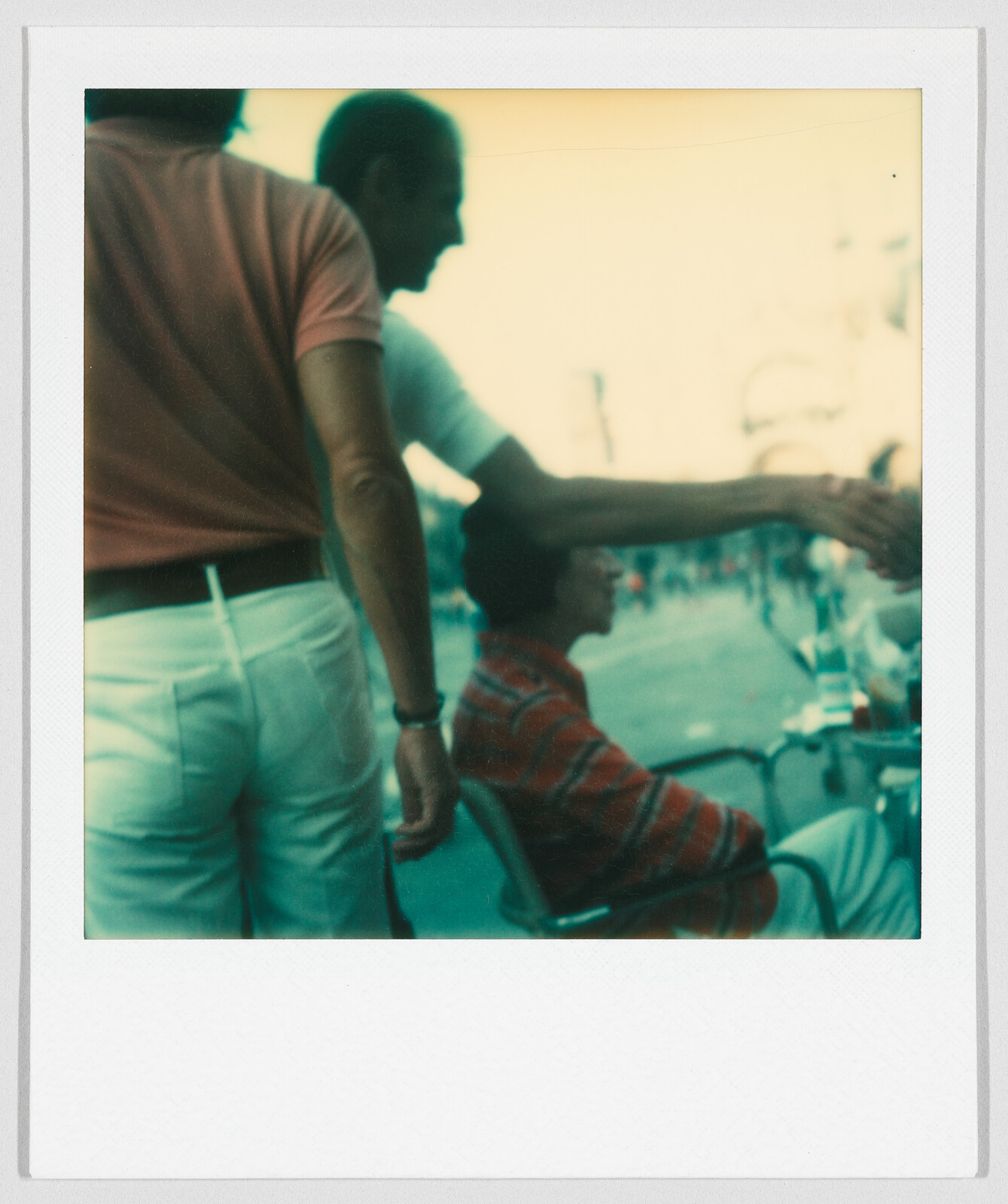 Two people standing and one person sitting outdoors, with one person reaching out to shake hands.