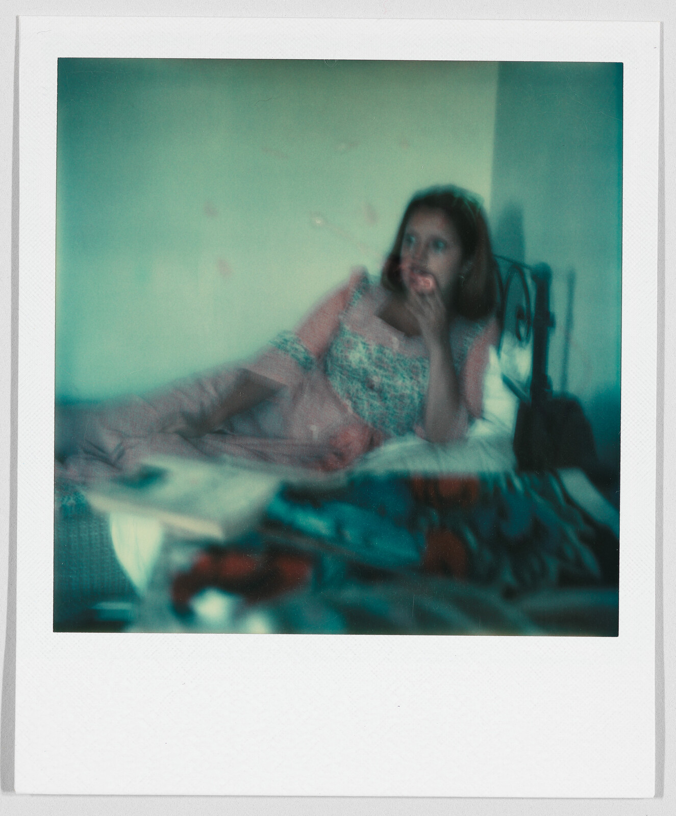 A woman in a patterned dress lies on a bed, resting her head on her hand, looking thoughtful.